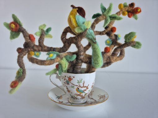 needle felted sculpture of bird in a teacup, brightly coloured felted bird sits in a many branched tree surveying the land from the vintage cup and saucer. brightly coloured leaves and flowers adorn the tree of this needle felted sculpture in a teacup.