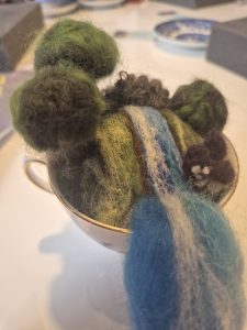 Needle felted landscapes in a teacup, blue wool river, green wool trees, vegetation.